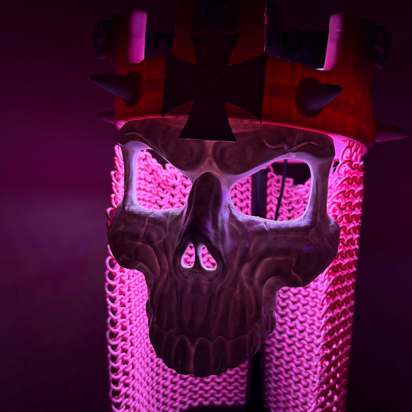 Close-up of the Skull King Crown and skull mask under purple-pink lighting, highlighting the sculpted skull detail and drape.